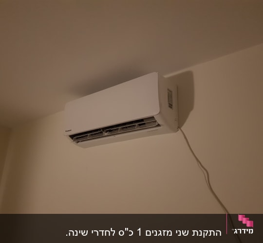 מזגן קיר לבן מותקן על קיר עם כבל חשמל